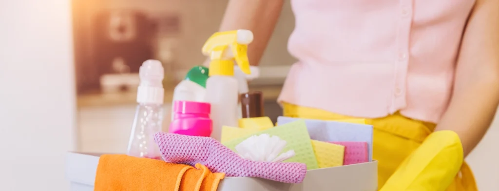 Limpeza segurando uma cesta cheia de produtos de limpeza coloridos, panos, escovas e frascos de spray.